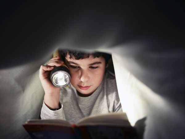 young-boy-school-child-reading-book-at-night-under-PDGBM54-2